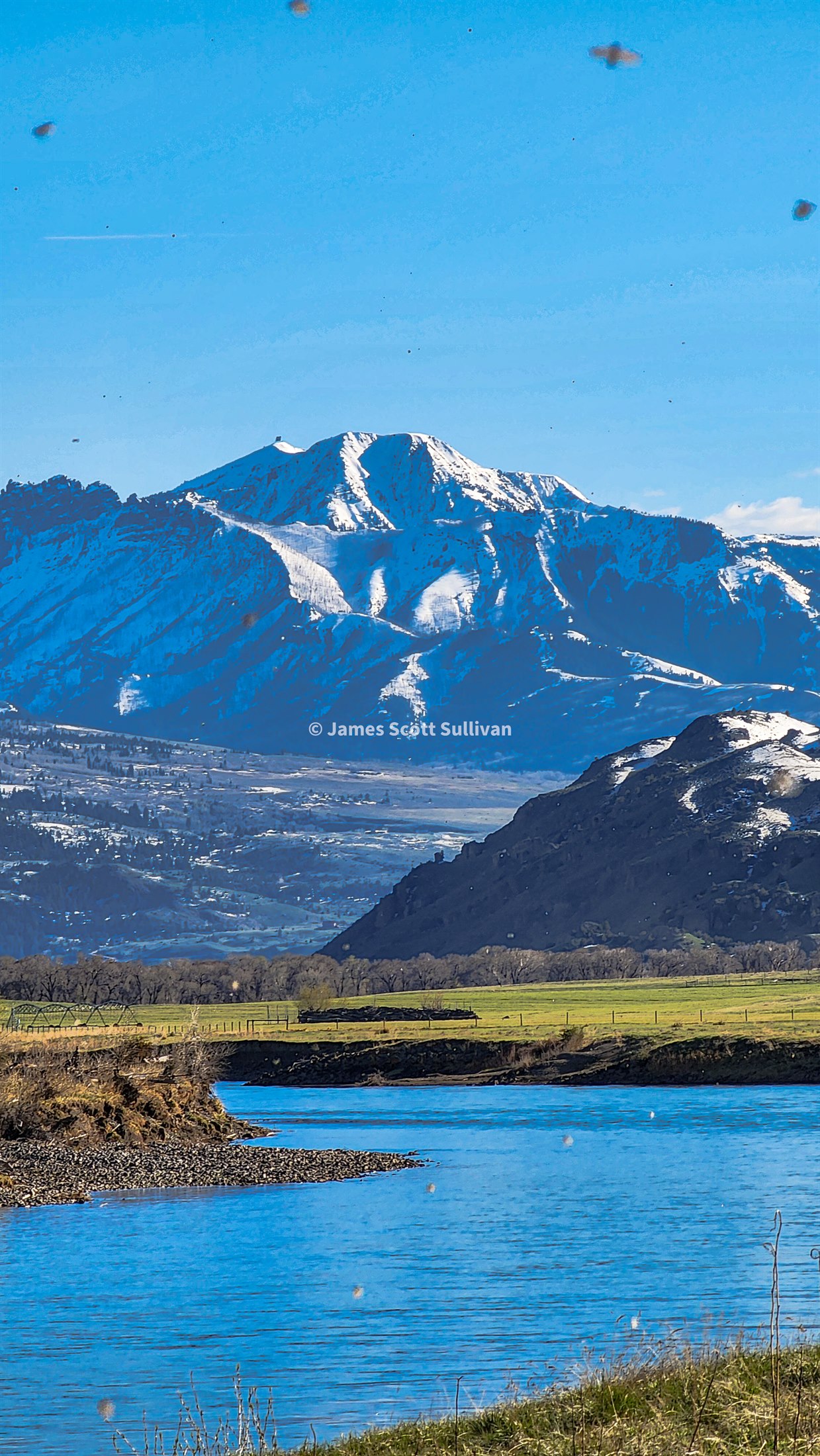 Snowy mountain above a blue river in Montana during the road trip.