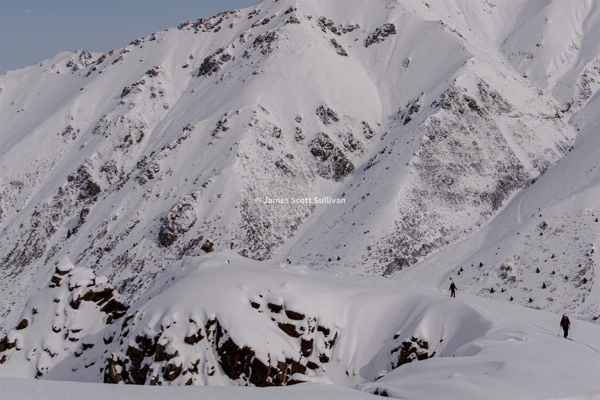 Two skiers traversing a snowy ridge in the Jyrgylan Highlands of Kyrgyzstan.